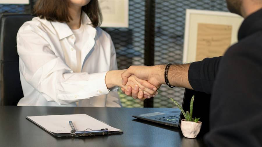 Two people shaking hands across a desk after an interview
