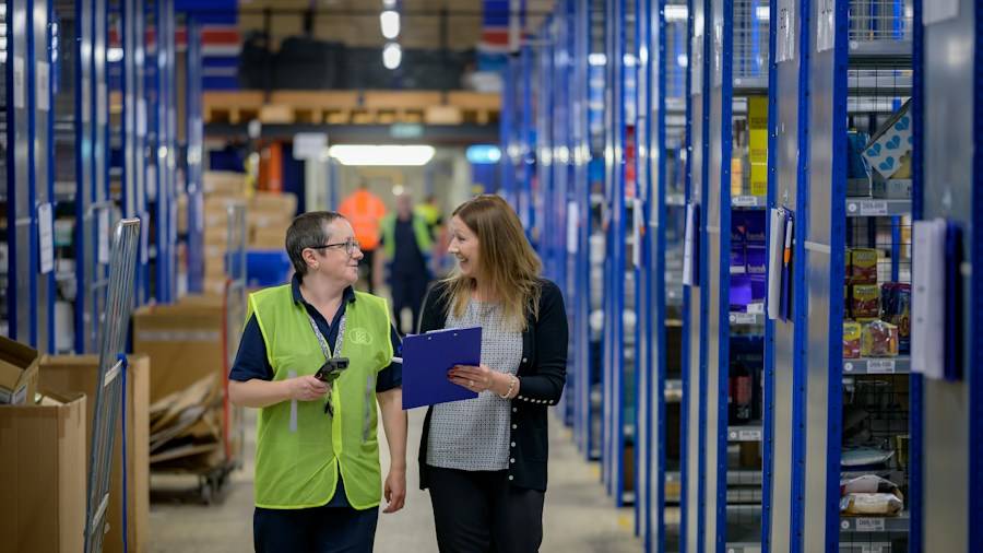 Two warehouse staff reviewing an order between shelving aisles