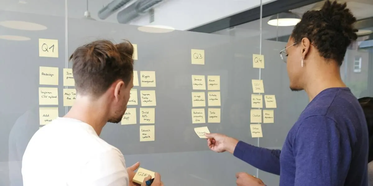 Two people planning a project with sticky notes on a glass wall